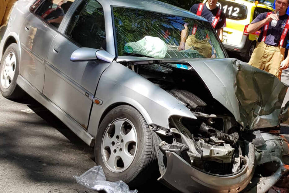 Einsatzkräfte betrachten das beschädigte Auto.