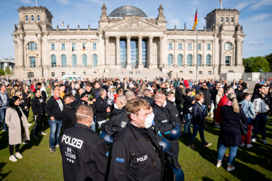 Polizeibeamte mit Mund-Nasen-Schutz stehen in einer Menschenmenge auf der Reichstagswiese vor dem Reichstagsgebäude.