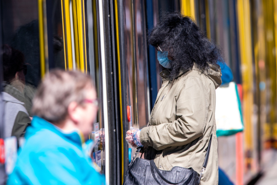 Eine Frau steigt in Schwerin mit Schutzmaske und Handschuhen in eine Straßenbahn ein. (Archivbild)