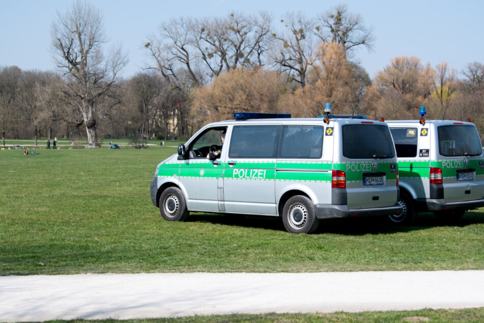 Zwei Polizeifahrzeuge stehen im Englischen Garten. Aufgrund der aktuellen Corona-Krise gelten in Bayern ab morgen weitreichende Ausgangsbeschränkungen.