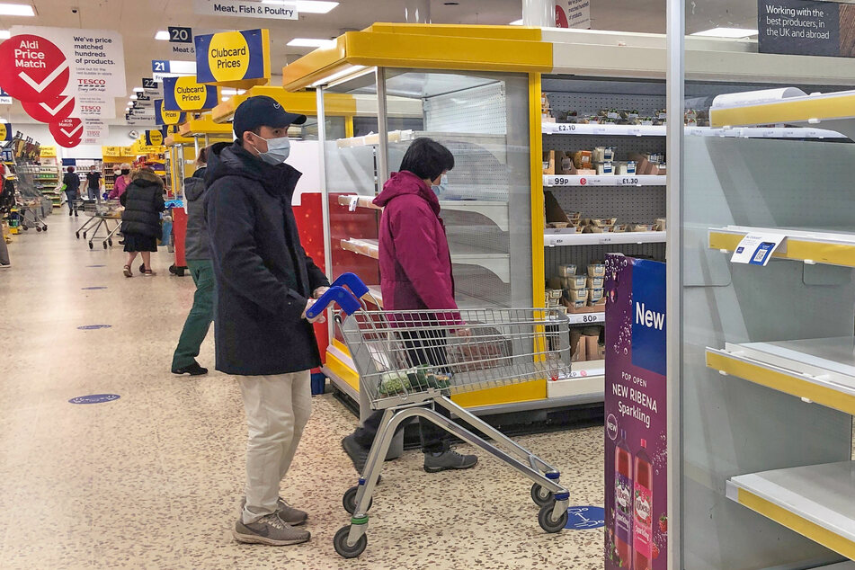 Ein Mann geht mit Maske durch einen Tesco-Supermarkt.