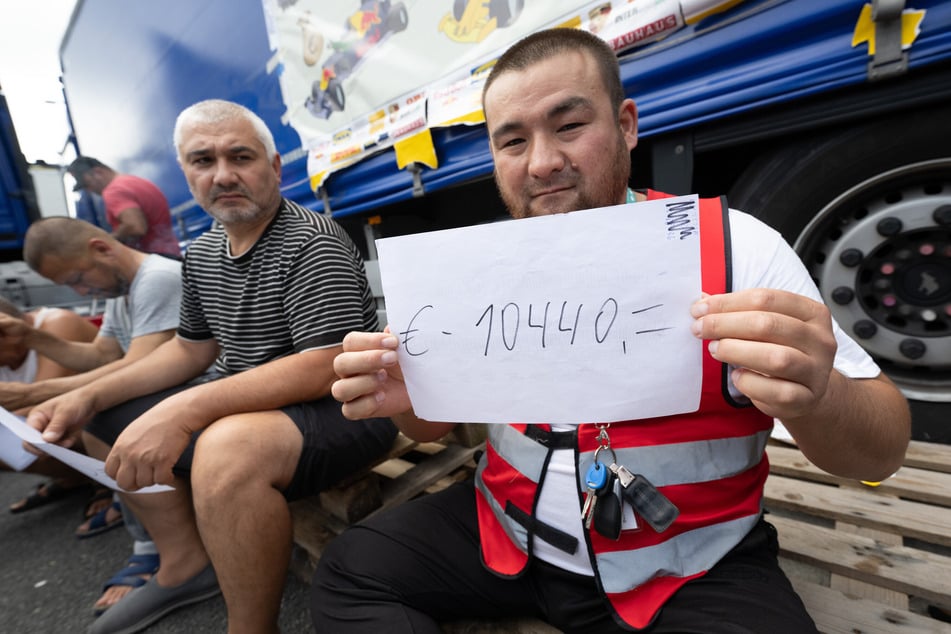 Ein LKW-Fahrer hält auf dem Parkplatz der Raststätte Gräfenhausen einen Zettel mit der Aufschrift "10.440 Euro" in den Händen, was den ihm bislang nicht ausgezahlten Lohn beziffern soll. Mittlerweile befinden sich die Trucker im Hungerstreik.