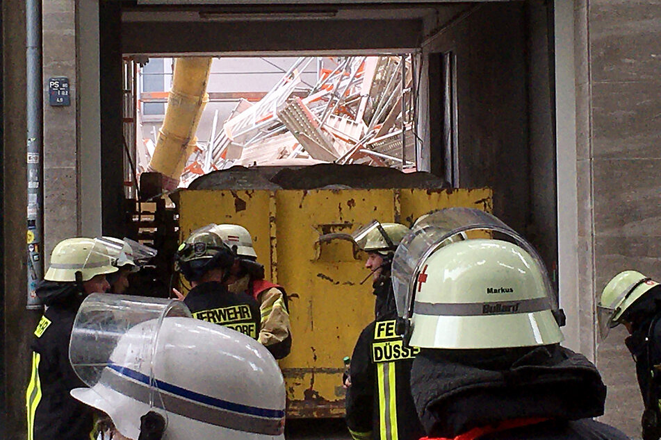 Einsatzkräfte der Feuerwehr stehen vor einer Hauseinfahrt, durch die ein eingestürztes Gerüst zu sehen ist.