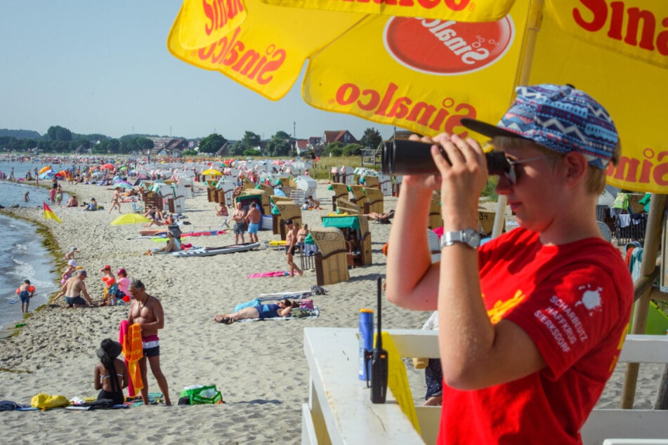 Eine Mitarbeiterin der DLRG Deutsche Lebens-Rettungs-Gesellschaft beobachtet einen mit Badegästen und Strandkörben gefüllten Strandabschnitt in Scahrbeutz.