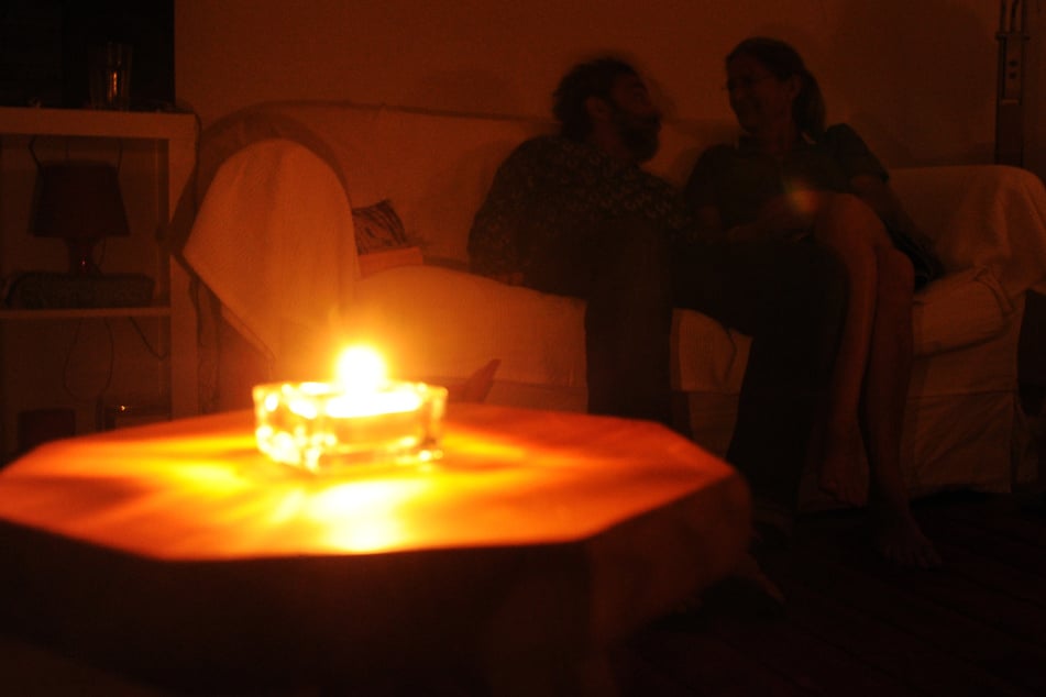 Ob ein Blackout so romantisch wird? Ein Paar sitzt während eines Stromausfalls bei Kerzenschein in einer Wohnung.