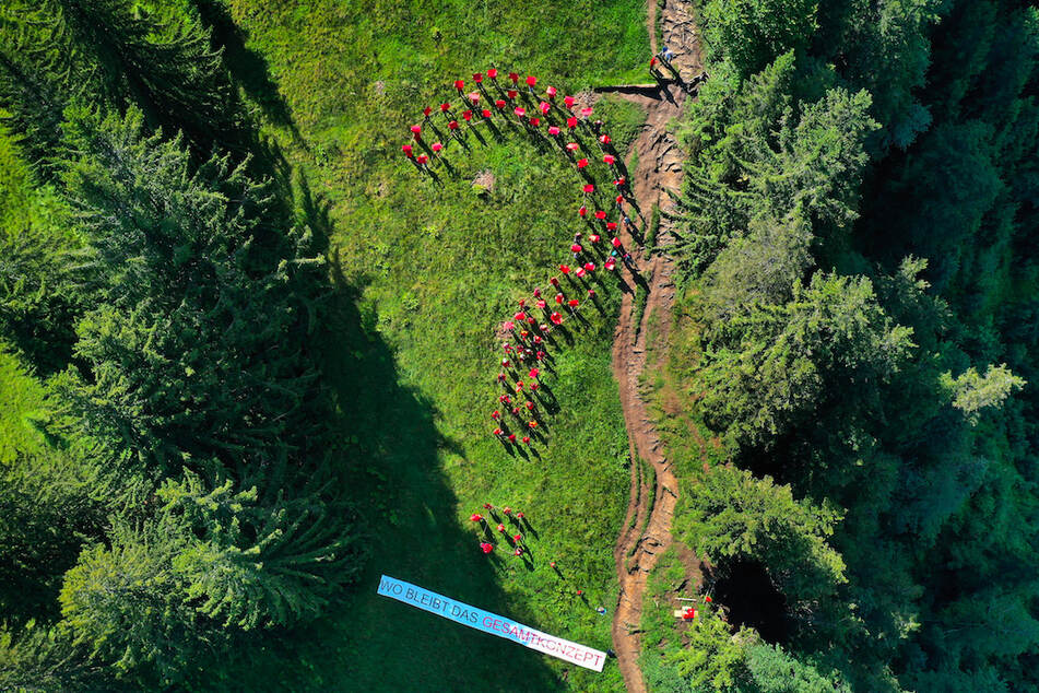 Rund 80 in Rot gekleidete Menschen stehen auf einer Bergwiese am Grünten in Form eines Fragezeichens über einem Plakat mit der Aufschrift "Wo bleibt das Gesamtkonzept".