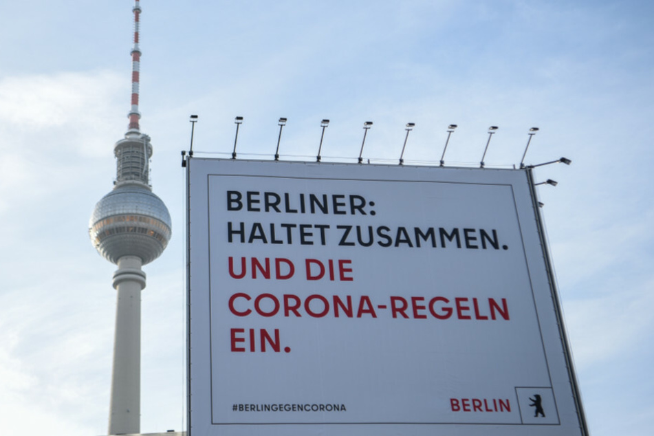 Vor dem Berliner Fernsehturm steht ein Plakat mit der Aufschrift "Berliner: Haltet zusammen. Und die Corona-Regeln ein."