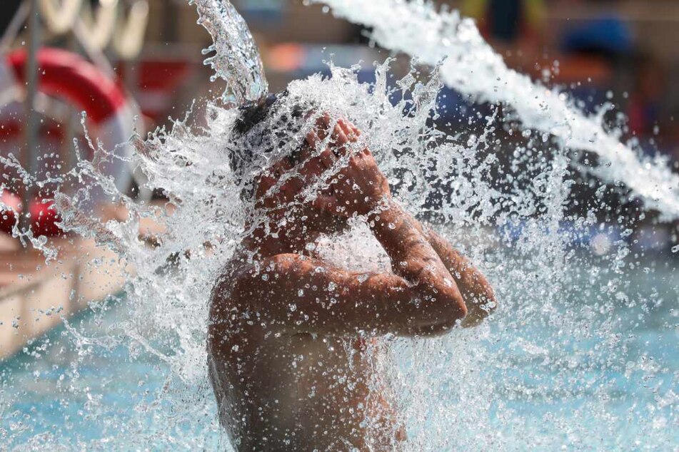 Sigmaringen: Ein Mann kühlt sich im Freibad unter einer Wasserfontäne ab.
