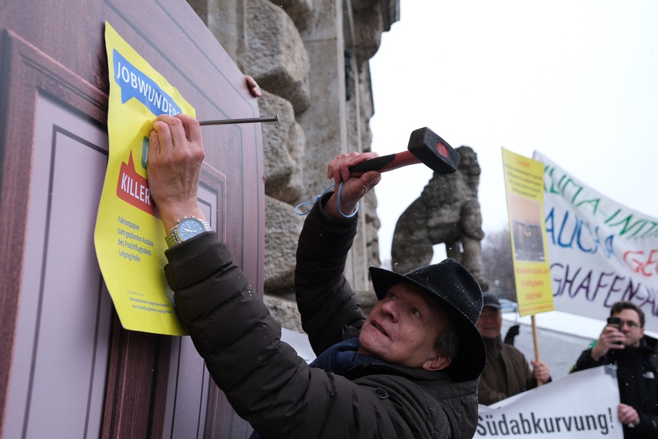 Mit Hammer und Nagel befestigten Umweltaktivisten am Mittwoch Protestplakate gegen den Ausbau des Flughafens Leipzig/Halle an eine symbolische Tür am Neuen Rathaus.