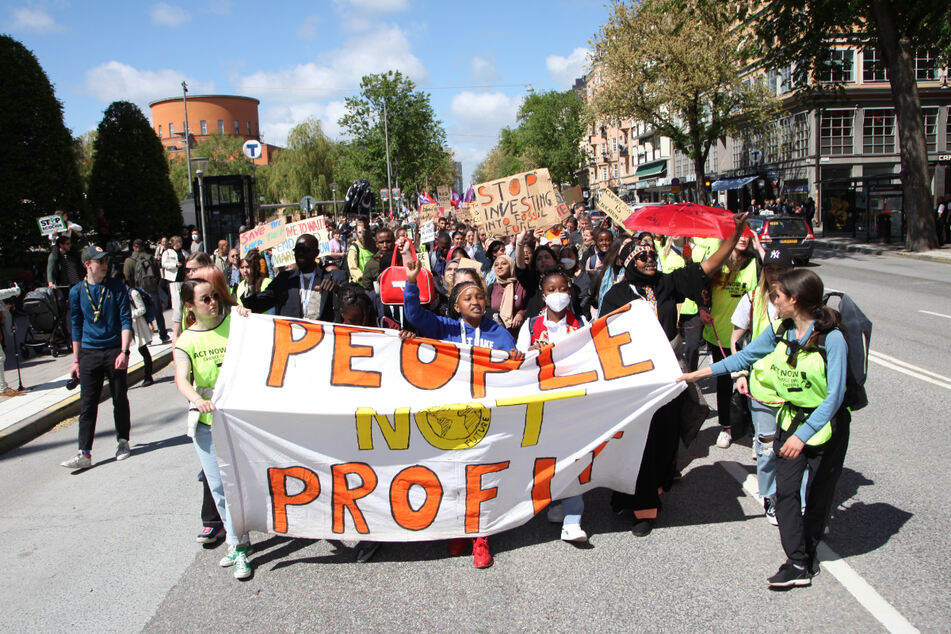 Demonstranten ziehen beim Klimaprotest anlässlich des Umweltgipfels Stockholm+50 durch die schwedische Hauptstadt und tragen dabei ein Transparent mit der Aufschrift "Menschen statt Profit".