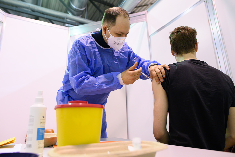 Ein Arzt impft im Impfzentrum in der Messe Dresden einen jungen Mann mit dem Astrazeneca-Wirkstoff gegen Corona.