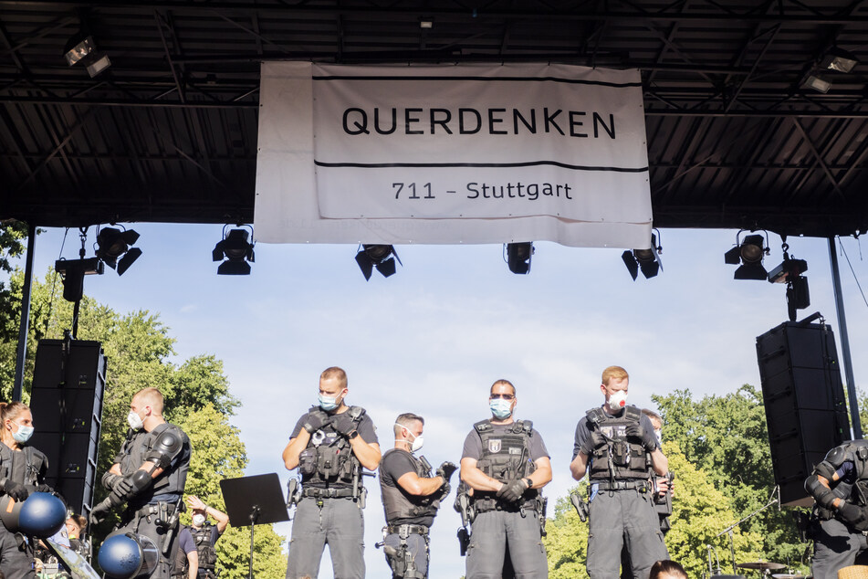 Polizisten stehen bei einer Kundgebung gegen die Corona-Beschränkungen auf der Straße des 17. Juni auf der Bühne unter einem Transparent der Initiative "Querdenken 711".