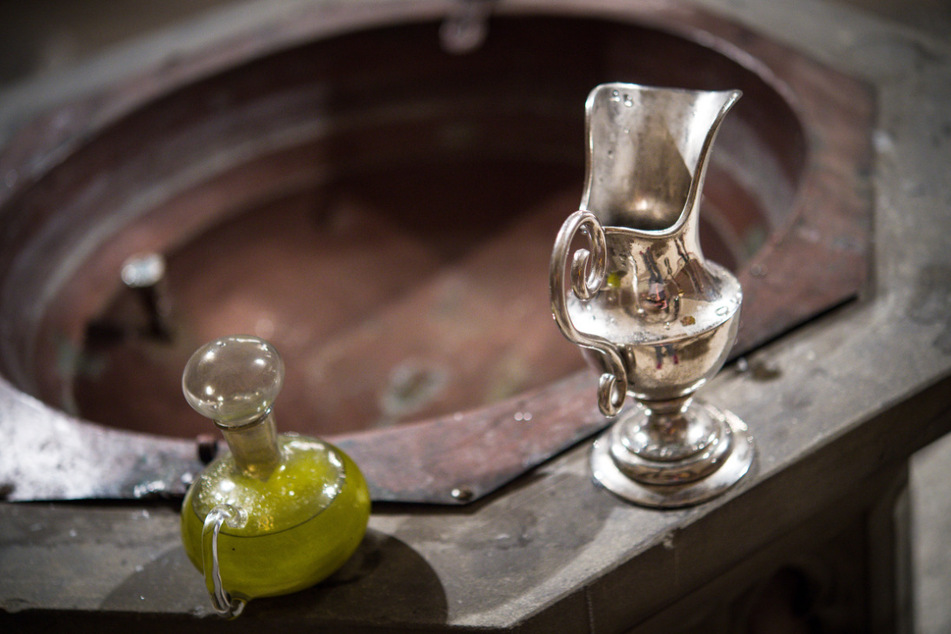 Eine Wasserkaraffe und Chrisamöl in einem Glasflakon stehen in der katholischen Kirche St. Josef in Bamberg am Rande des Taufbeckens für eine Taufe bereit.