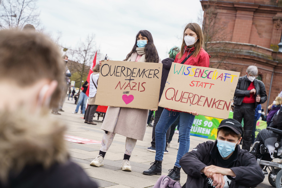Zwei Demonstrantinnen gegen eine Kundgebung der "Querdenken"-Bewegung halten vor dem Bahnhof Plakate mit der Aufschrift "Querdenken + Nazis = (Herz)" und "Wissenschaft statt Querdenken".