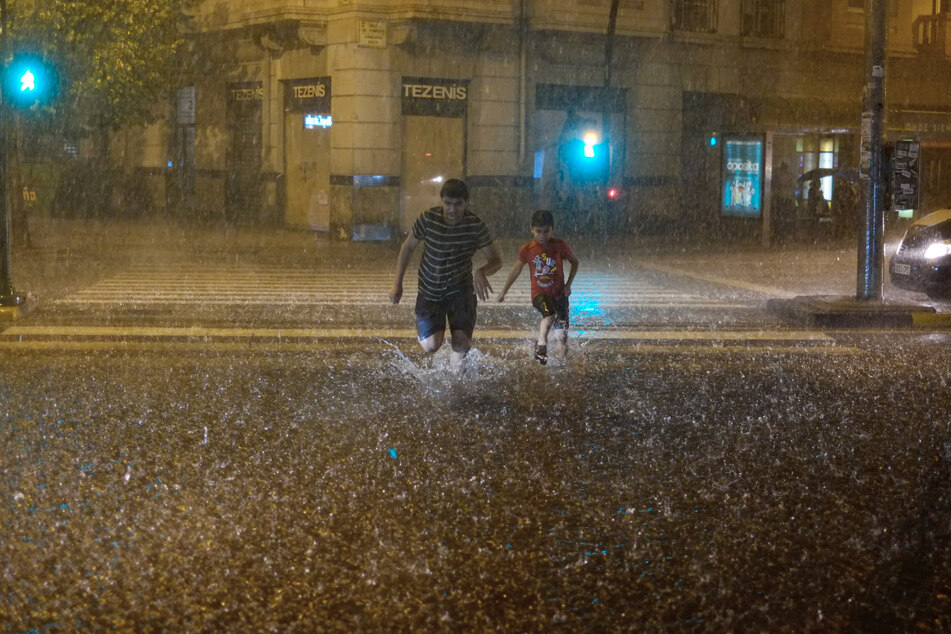 Schwere Regenfälle in Spanien: Menschen überqueren bei starkem Regen eine überschwemmte Straße in Pamplona.
