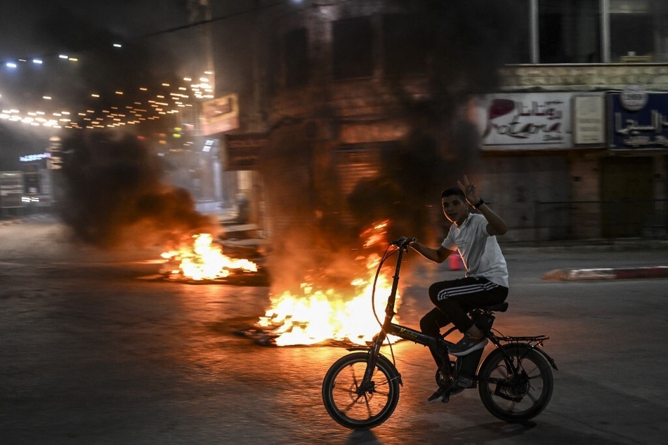 A Palestinian youth rides his bicycle next to burning tires during an Israeli raid on the occupied West Bank city of Jenin on May 21, 2024.