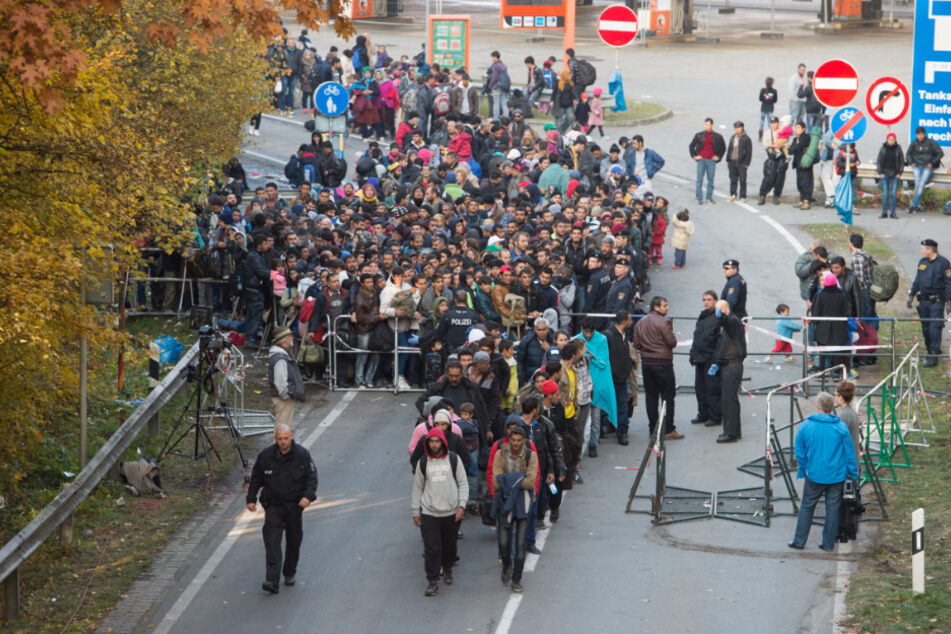 Flüchtlinge überqueren nahe Passau neben einem Polizisten die deutsch-österreichische Grenze. (Archiv)