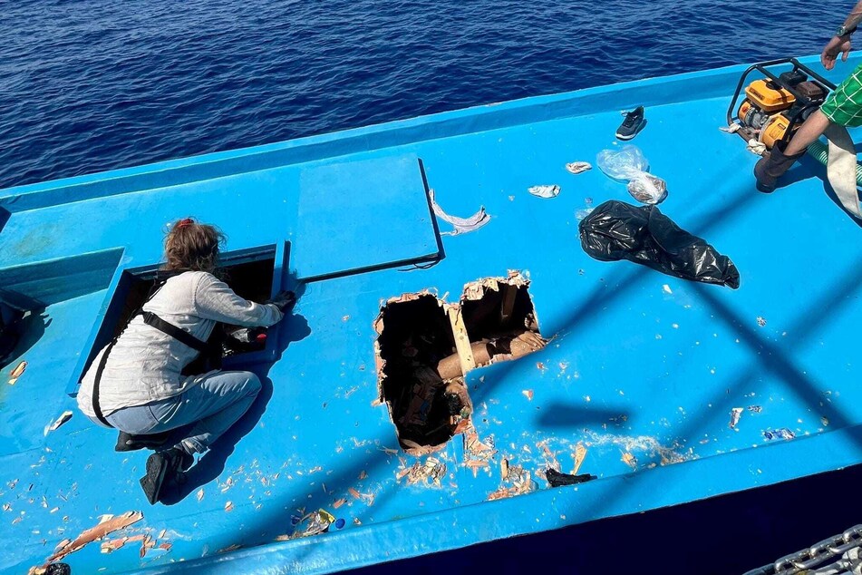 Mitglieder der Besatzung des deutschen Motorsegelschiffs "Nadir" legen mit einer Axt den Weg zum Unterdeck eines Migrantenbootes im Mittelmeer frei.