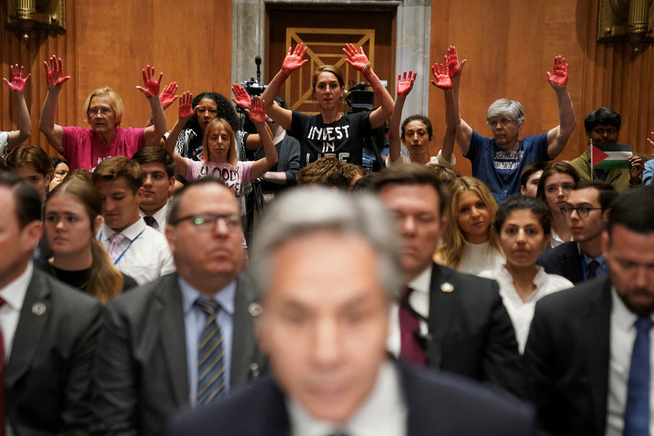 Pro-Palestine protesters hold up painted "bloody hands" as Secretary of State Antony Blinken testifies before the Senate Foreign Relations Committee.