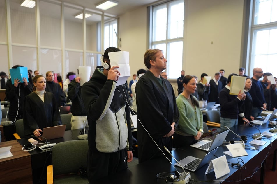 Die zehn Angeklagten stehen im Gerichtssaal neben ihren Anwälten im Prozess wegen besonders schweren Raubes mit Todesfolge.