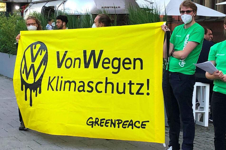 Demonstranten von Greenpeace stehen mit einem Poster "VW - Von Wegen Klimaschutz!" vor einer Halle, in der eine Veranstaltung von Volkswagen stattfand.