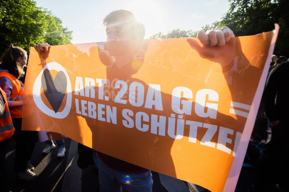 Ein Teilnehmer einer Demonstration der Letzten Generation hält bei der Abschlusskundgebung am Brandenburger Tor ein Banner hoch.