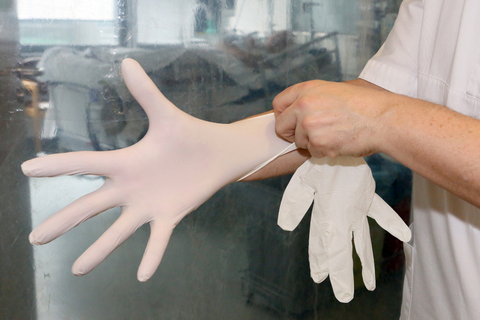 Ein Pfleger auf der Intensivstation in einem Krankenhaus zieht sich Handschuhe an.