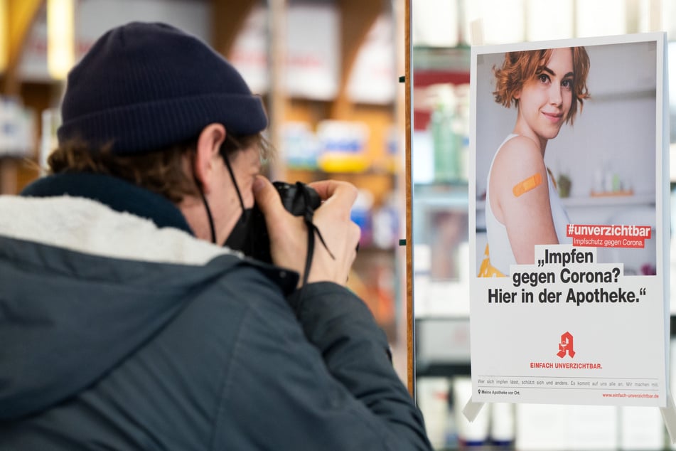 Ein Mann fotografiert ein Plakat, das in einer Apotheke auf das Impfen gegen Corona in der Apotheke hinweist.