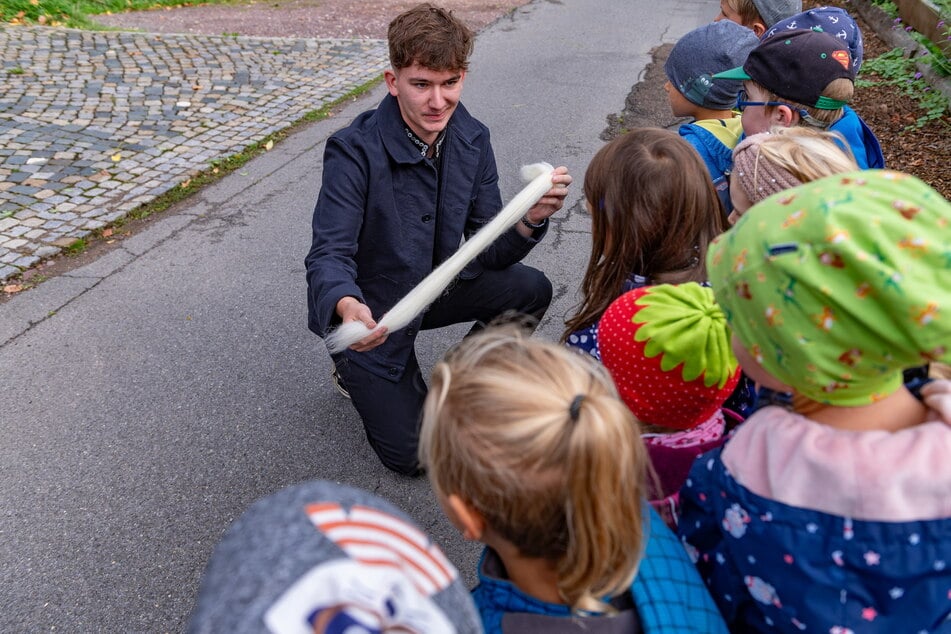 Julius Drutschmann erklärt hier Kindern der Kita Schloss-Spatzen, wie aus Wolle Kleidung wird.