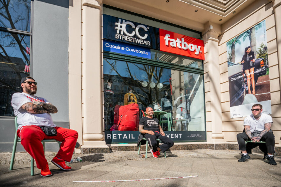 Drei Mitarbeiter eines geschlossenen Geschäfts für Streetwear sitzen vor ihrem Laden am Kurfürstendamm.