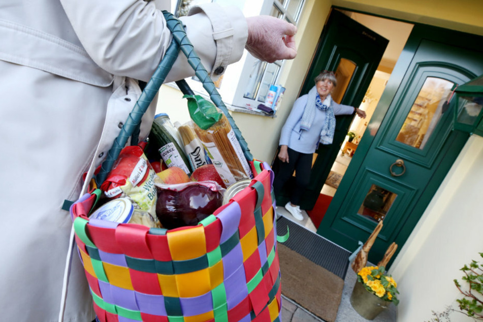 Nordrhein-Westfalen, Essen: Die 79jährige Inge Vincents (r) bekommt von ihrer Nachbarin Heike van Ackern eine Tasche mit den von ihr bestellten Lebensmitteln. Die Rentnerin möchte während der Corona-Pandemie wegen des erhöhten Ansteckungsrisikos möglichst ihr Haus selten verlassen.