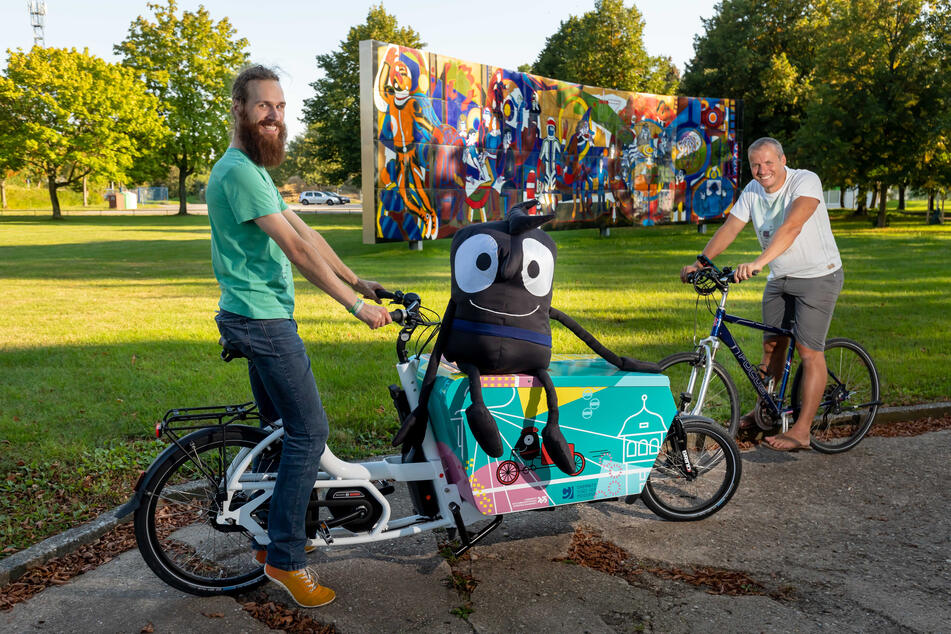 Die Mobitag-Organisatoren Bjarne Lotze (27, l.) und Marc Stoll (41) fahren mit Mobilitätswoche-Maskottchen Edgar Rad im Sportforum.