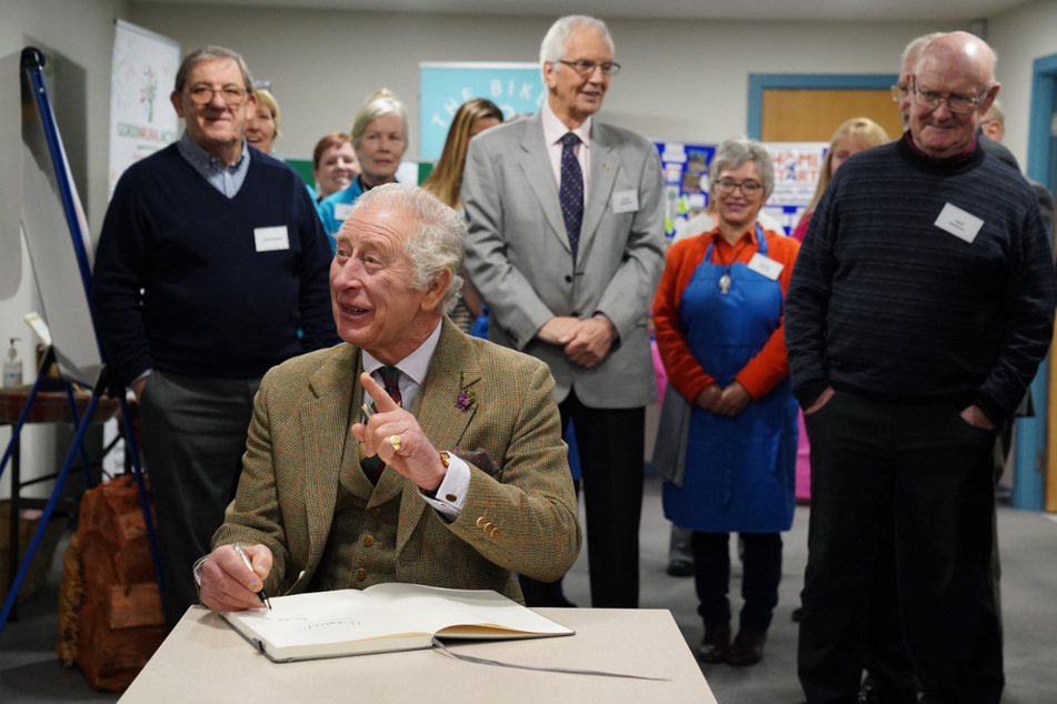 König Charles gestikuliert, als er sich während seines Besuchs des Gemeindezentrums Aboyne und Mid Deeside Community Shed in ein Buch einschreibt.