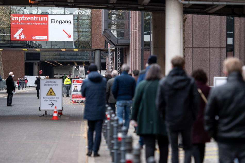 Menschen warten vor einem Kölner Impfzentrum. Die Verlängerung der Corona-Schutzverordnung in NRW soll die Zeit überbrücken, bis bundeseinheitliche Regelungen greifen.