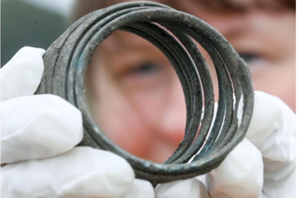 Eine Grabungstechnikerin zeigt eine bronzene Armspirale aus der Zeit der Himmelsscheibe von Nebra in Friedrichsschwerz bei Halle. Der Schmuck lag als Beigabe in einem Grab mit einem Baby.