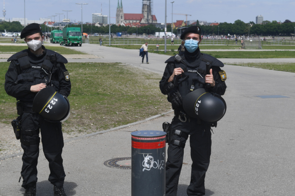 Polizisten stehen mit ihrer Schutzausrüstung an der Theresienwiese. Sperrgitter teilen die Wiese auf.