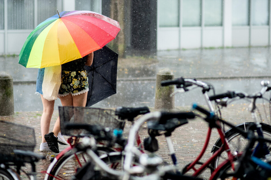 Zwei Frauen suchen unter einem bunten Schirm Schutz vor dem Regen.