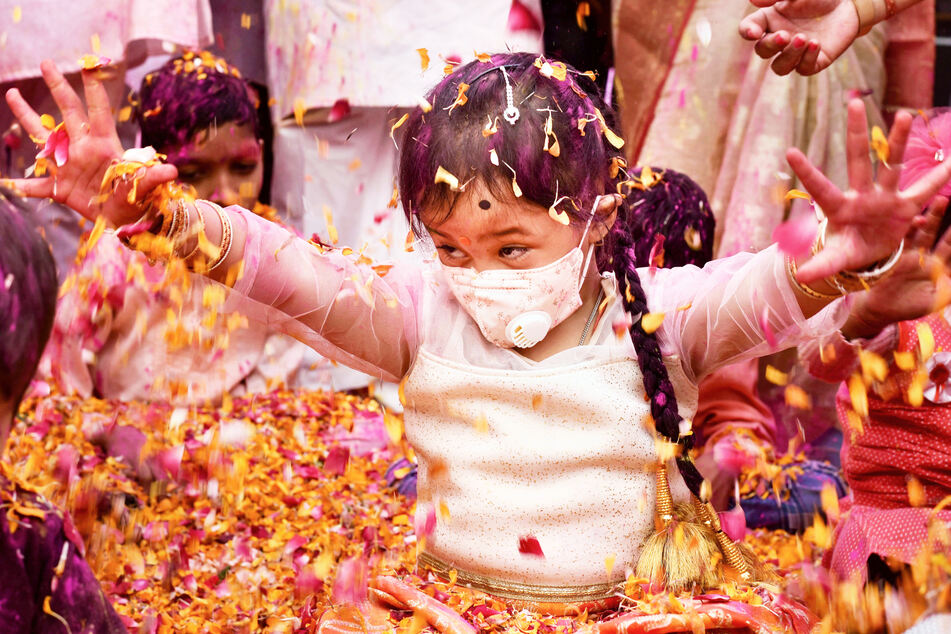 Ein Kind mit Mundschutzmaske sitzt während der Holi-Feierlichkeiten der Trishala-Stiftung in Prayagraj, Indien, inmitten von Blüten.