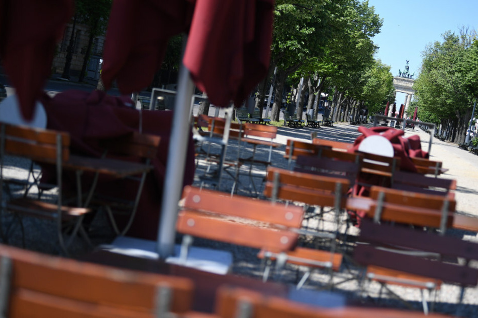 Leere Stühle und Tische stehen Unter den Linden vor dem Brandenburger Tor im Außenbereich eines Cafés.