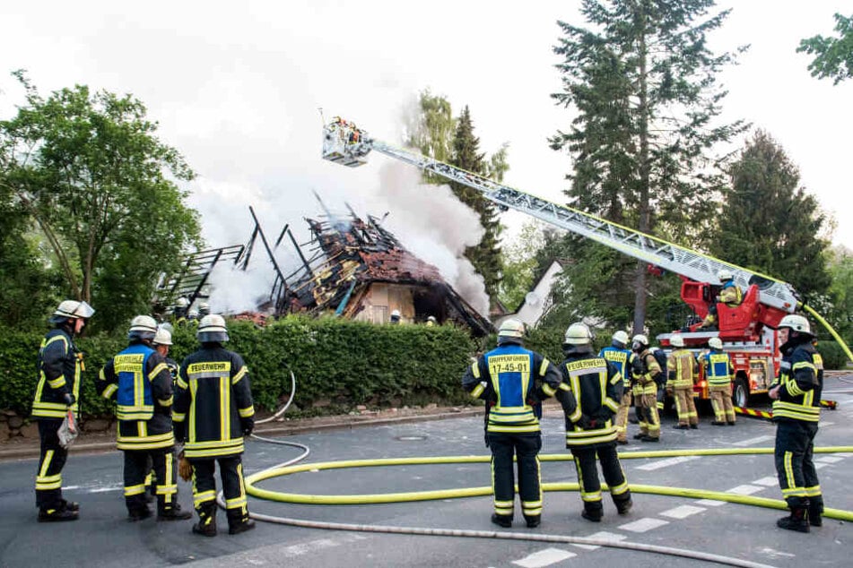 Feuerwehrleute stehen vor dem zerstörten Wohnhaus, aus dem dicker Rauch aufsteigt.