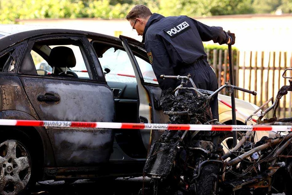 Ein Polizist steht an den ausgebrannten Fahrzeugen in Prohlis.