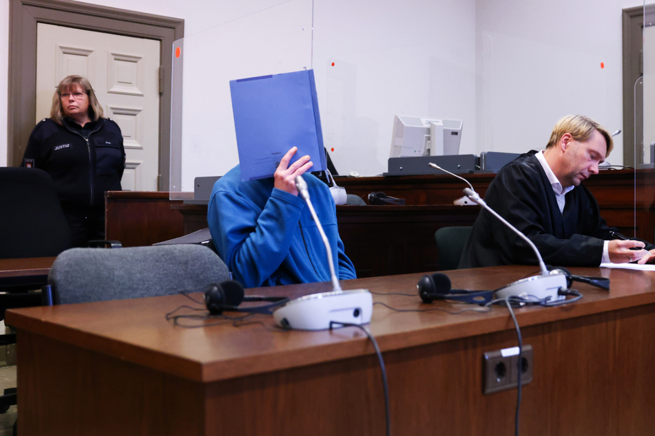 Der Angeklagte (M.) sitzt neben seinem Anwalt Philipp Naumann (r.) zu Beginn des Prozesses im Strafjustizgebäude.