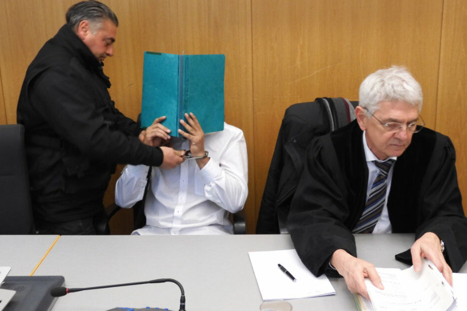 Ein Justizbeamter nimmt im Gerichtssaal dem Angeklagten die Handfesseln ab.