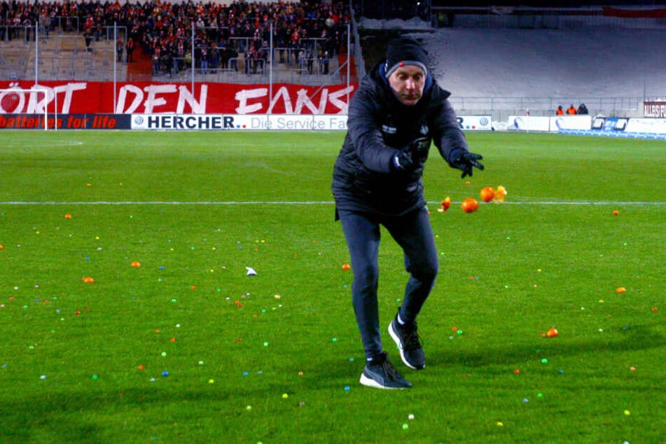 Zwickaus Mannschaftsleiter Mario Kallisch entsorgt die von Eintracht-Anhängern aufs Feld geworfenen Mandarinen.