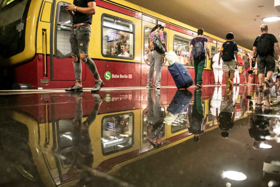 Berliner und Touristen laufen auf dem nassen Bahnsteig des Bahnhofs Friedrichstraße.