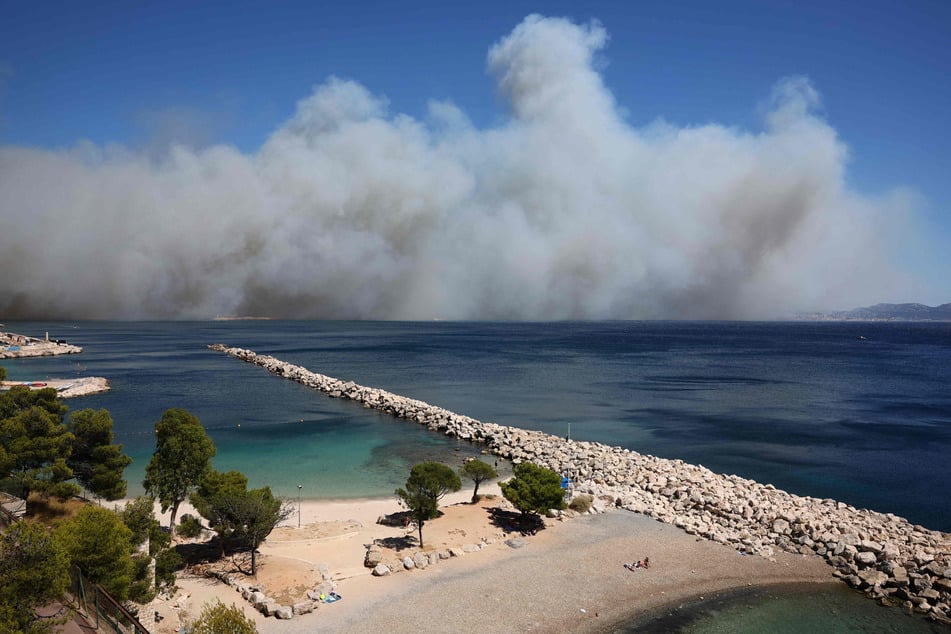 Sonnenanbeter liegen am Plage des Corbieres am Stadtrand von Marseille in Südfrankreich, während im Hintergrund der Rauch eines Flächenbrandes wütet.