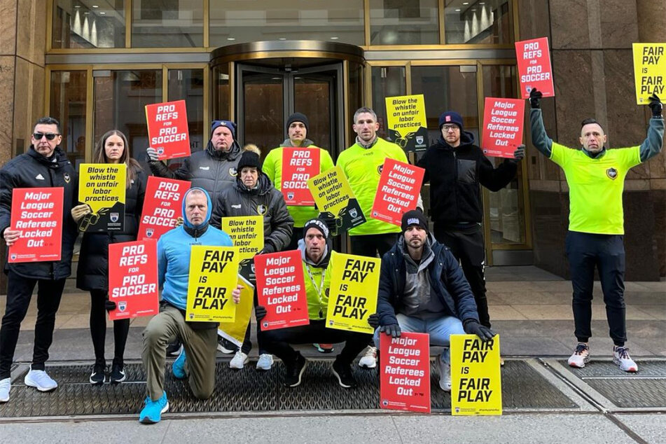 Striking Major League Soccer referees picket in New York City, raising signs reading "Fair Pay is Fair Play" and "Pro Refs for Pro Soccer."