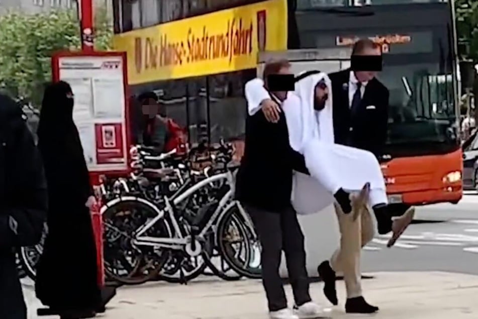 Angestellte tragen den Scheich auf Händen zu seinem Auto.