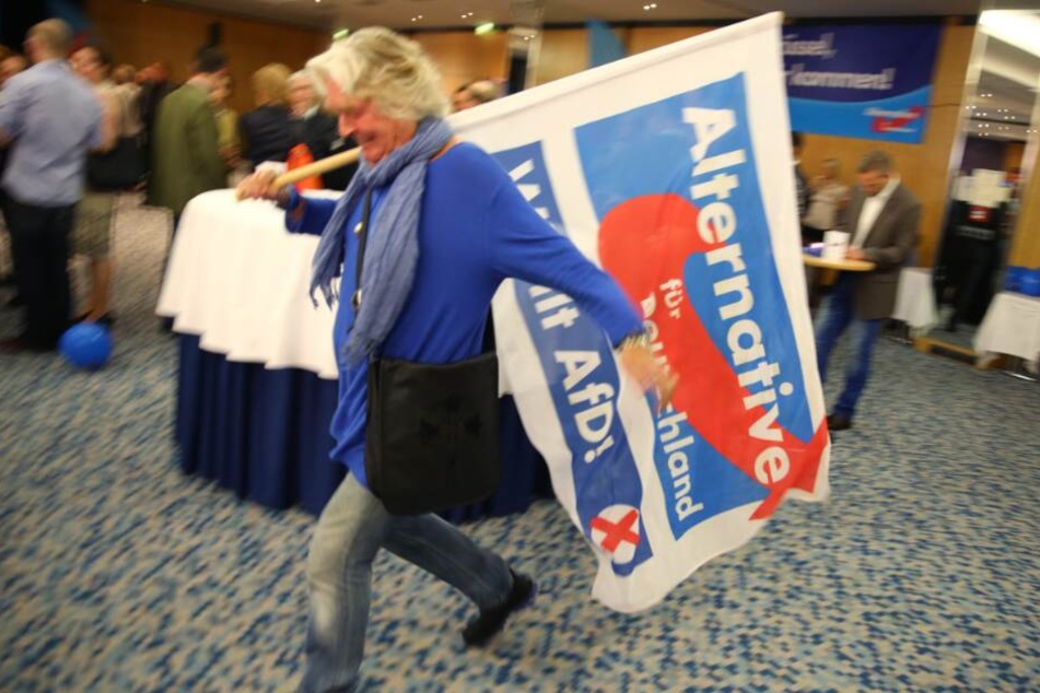 Eine Anhängerin der AfD schwingt eine Fahne ihrer Partei.