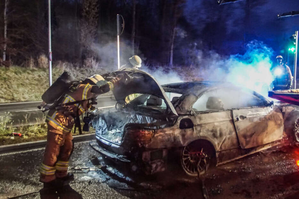 Ein Feuerwehrmann begutachtet den ausgebrannten BMW.